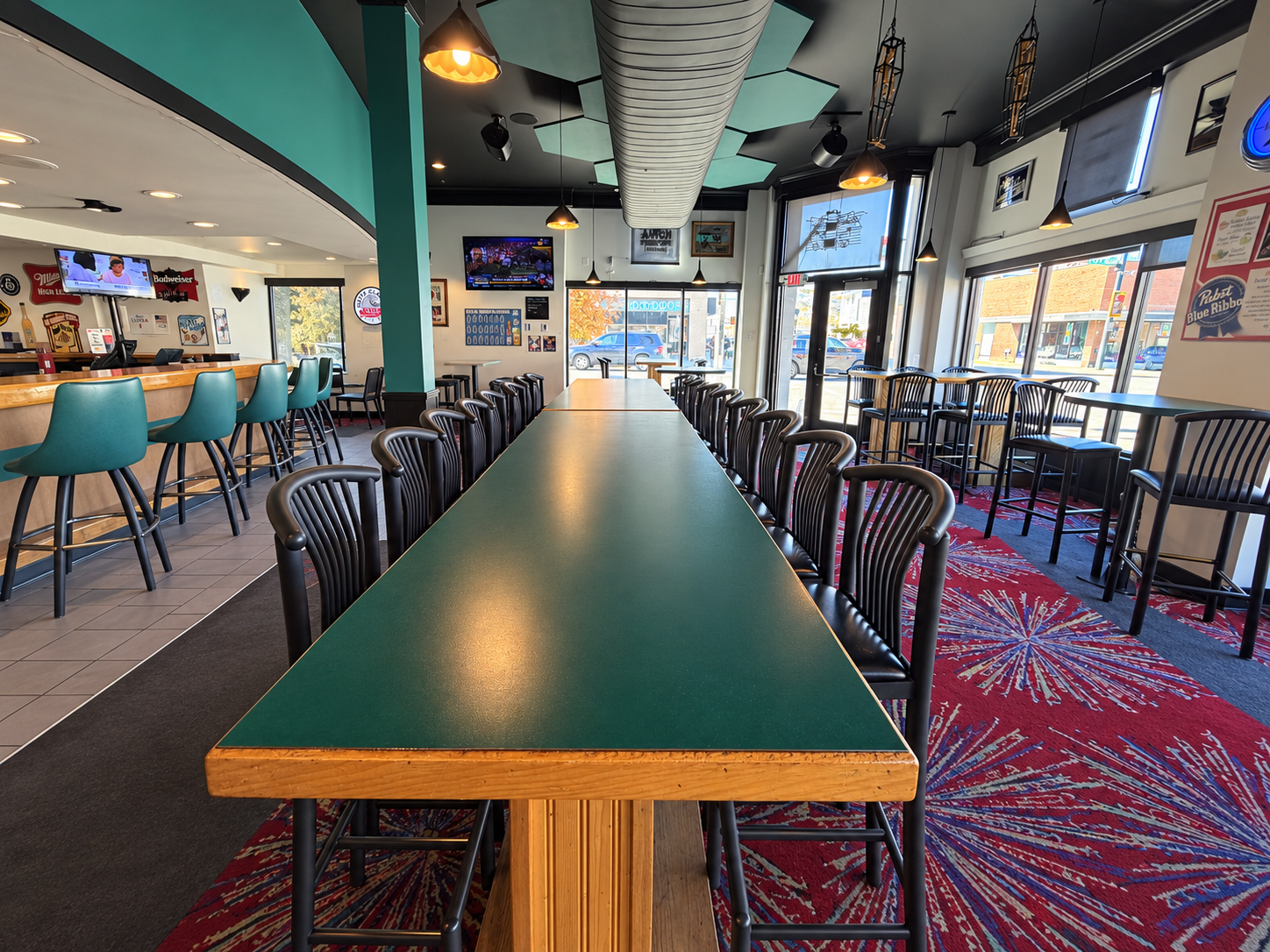 A long communal table with aligned chairs beside The Monte’s teal bar seating